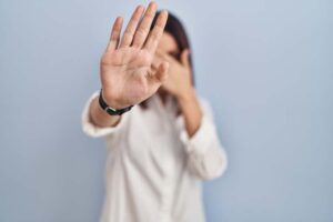 Young hispanic woman standing over white background covering eyes with hands and doing stop gesture with sad and fear expression. embarrassed and negative concept.